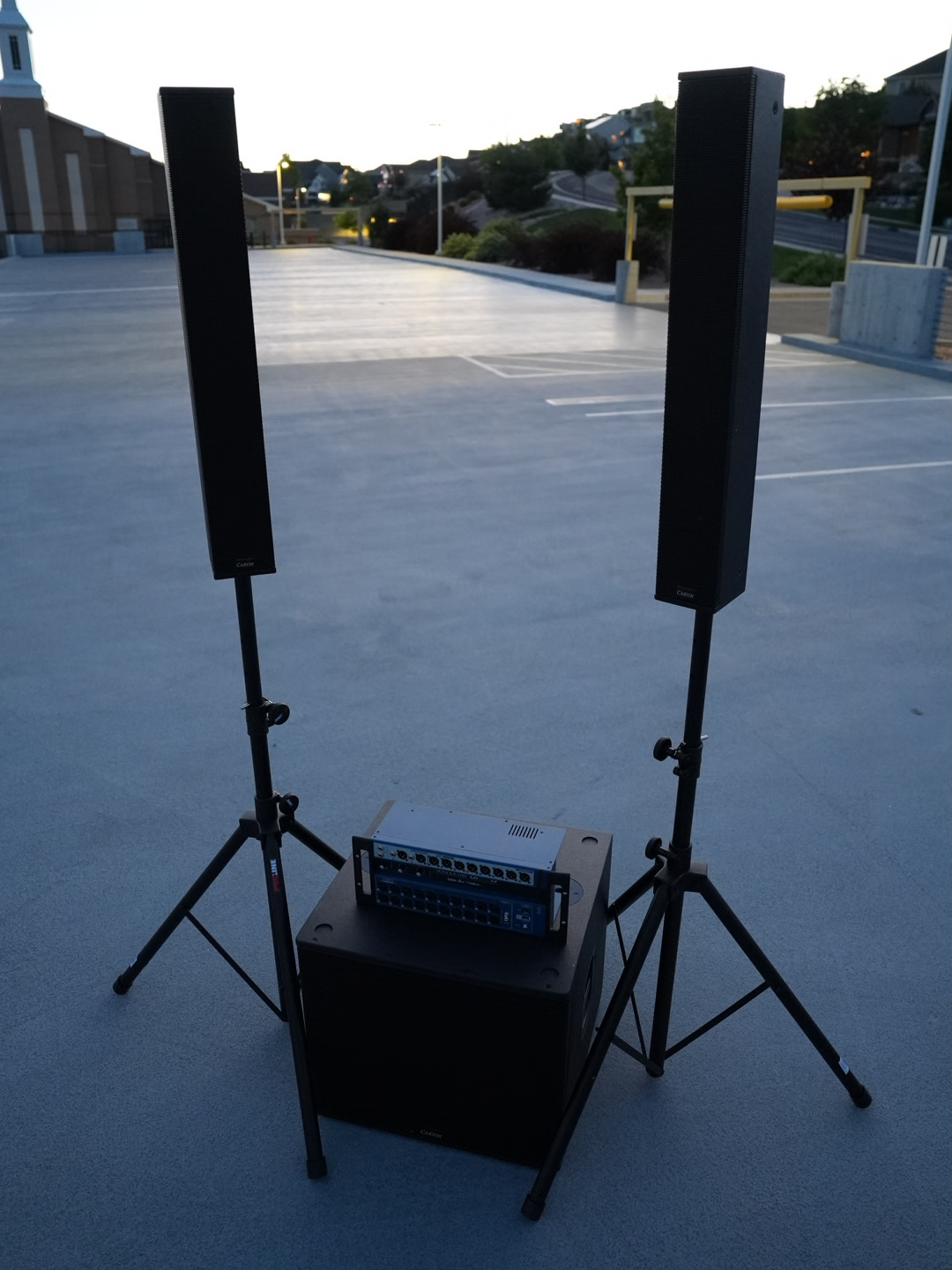 Column array speakers and a mixer staged outside a church at dusk