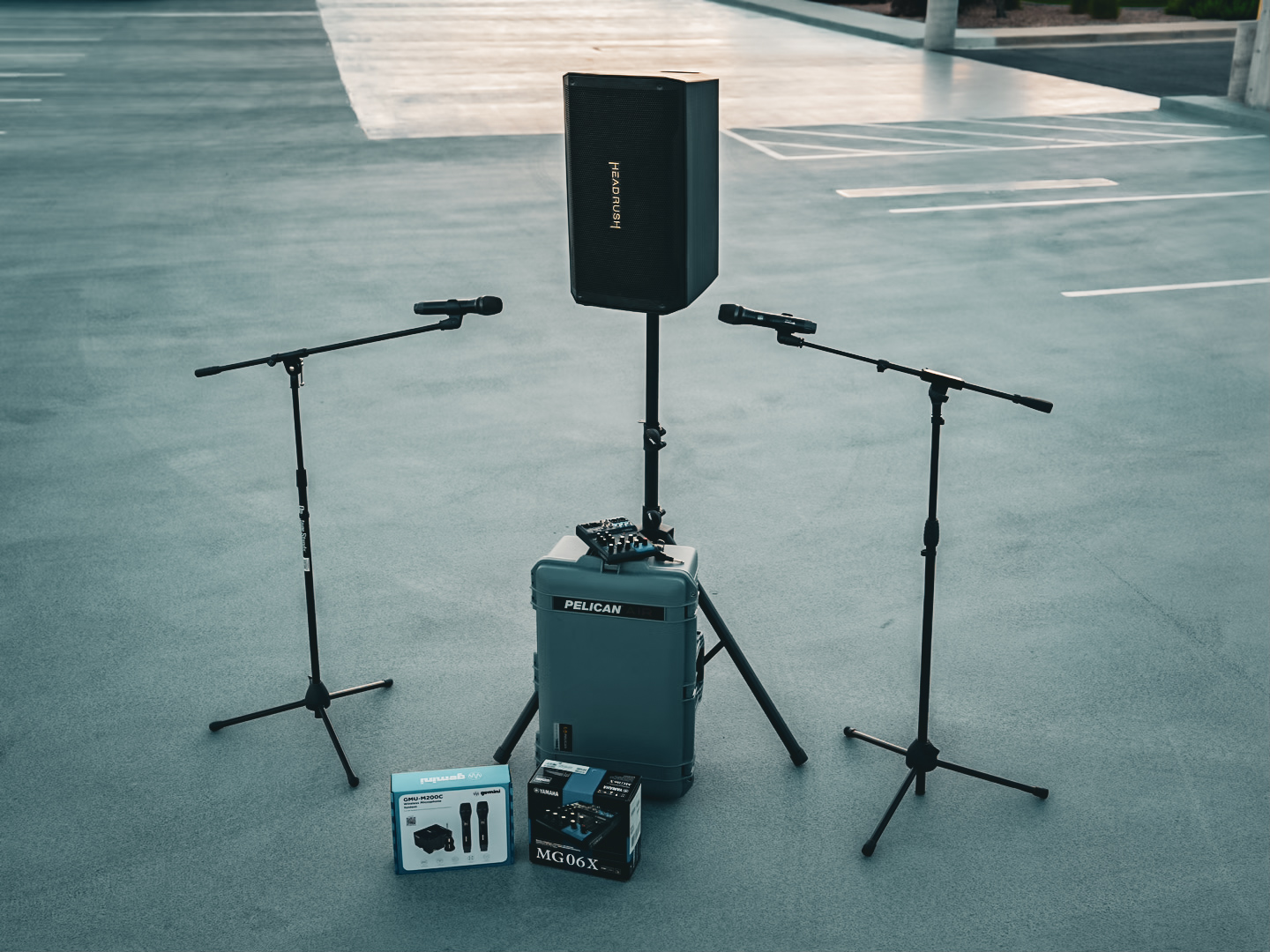 A small-event rental kit laid out: a powered speaker on a stand, two handheld microphones on boom stands, a Pelican road case, and a Yamaha mixer