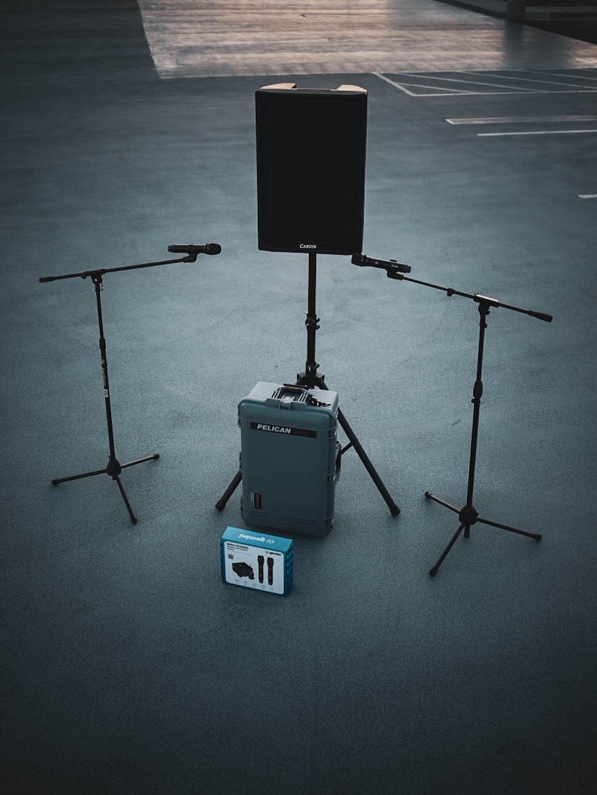 A Carvin powered speaker and two microphone stands arranged around a Pelican case