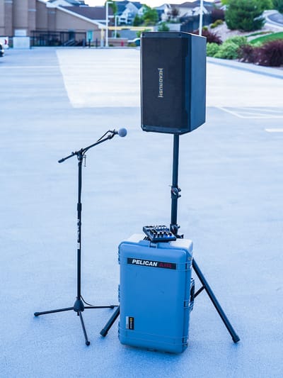 A HeadRush powered speaker on a stand beside a boom microphone stand, with a Yamaha mixer resting on a Pelican Air case