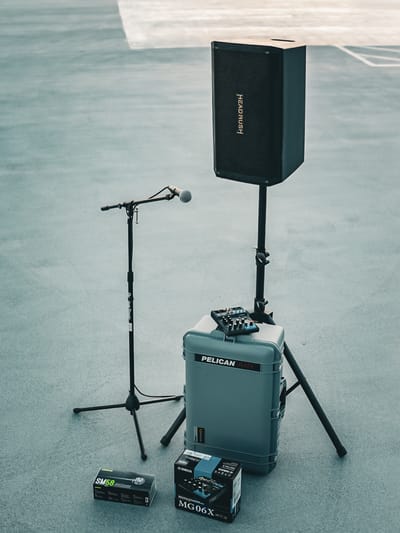 A wired microphone on a boom stand beside a powered speaker, a Yamaha mixer, and a boxed Shure SM58