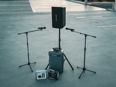 A small-event rental kit laid out: a powered speaker on a stand, two handheld microphones on boom stands, a Pelican road case, and a Yamaha mixer