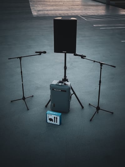 A single Carvin speaker on a stand flanked by two microphone stands, with a mixer and Pelican Air case at its base