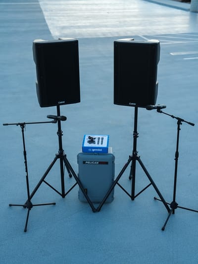 A stereo pair of Carvin speakers on stands with a microphone stand outside each of them and a mixer case between