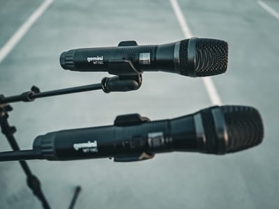Two Gemini MT10C wireless handheld microphones clipped into boom stands