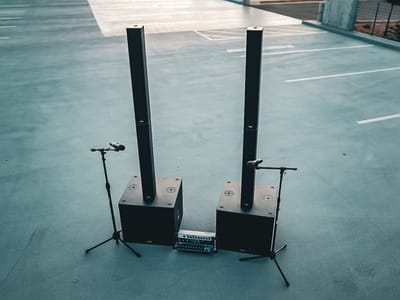 Two subwoofers each topped with a column array, a Soundcraft Ui24R mixer on the ground between them, and a wireless microphone on a stand at either side