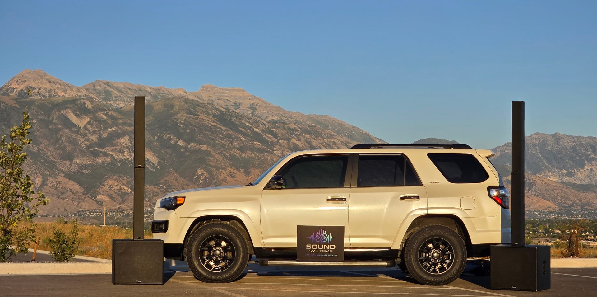 A column array standing on a powered subwoofer at each end of the branded Sound Systems SUV, the Wasatch range behind them at golden hour
